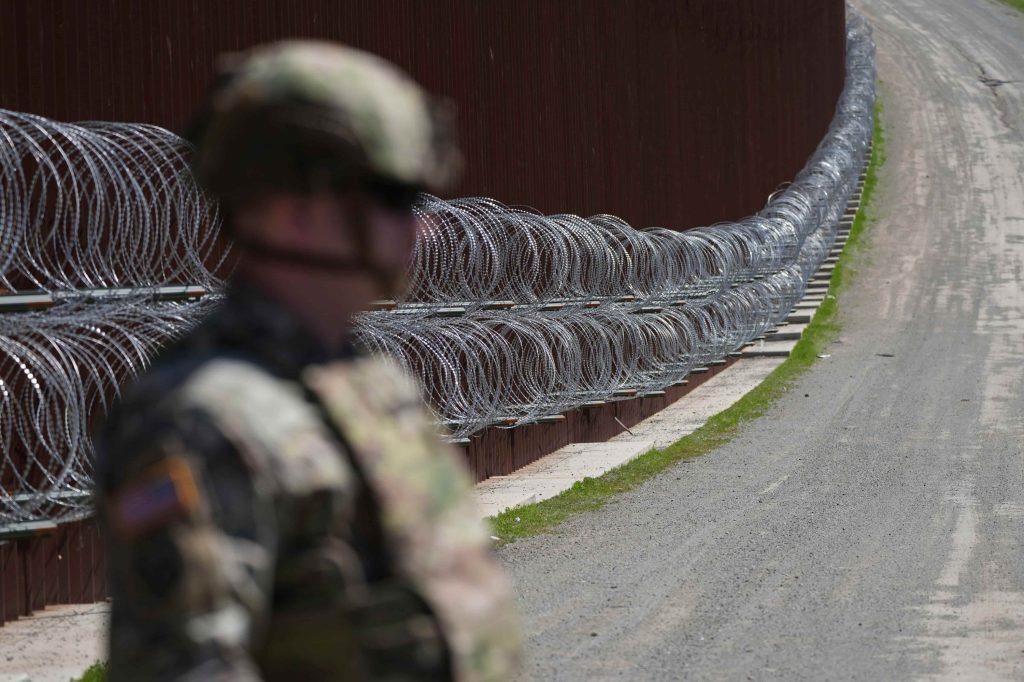 A member of the military looks on in front of newly-installed concertina wire lining one of two border walls separating Mexico from the United States during a news conference on joint operations involving the military and the Border Patrol Friday, March 21, 2025, in San Diego. (AP Photo/Gregory Bull)