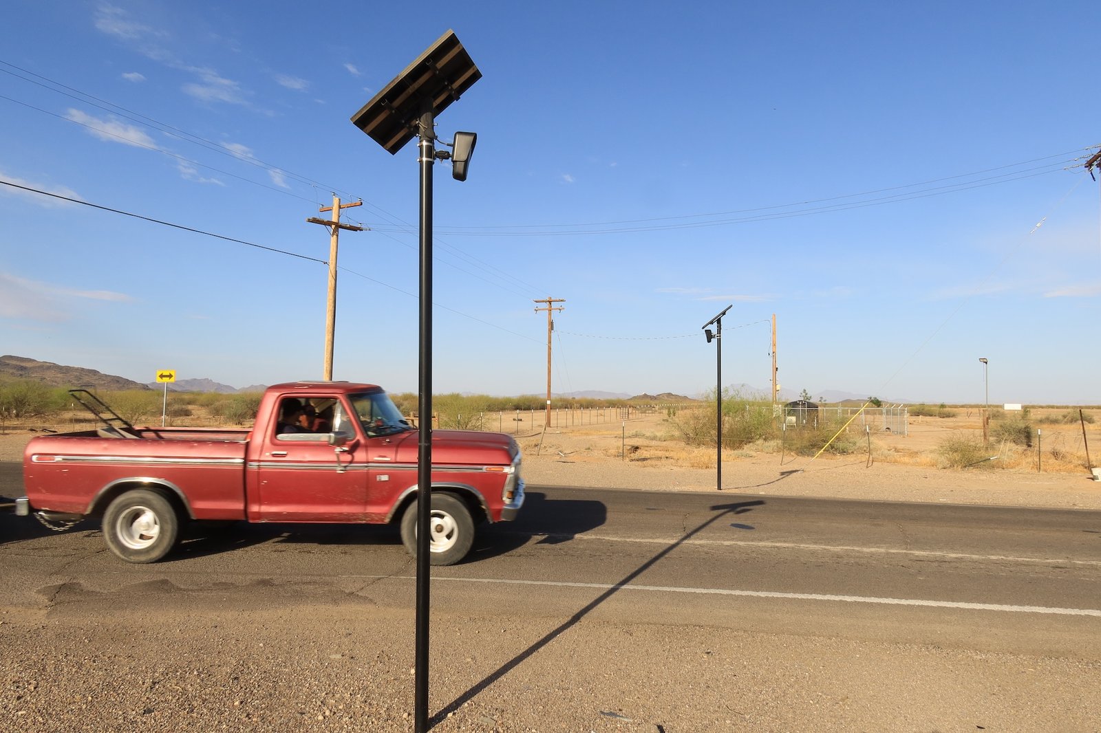A red truck passed a pair of Flock Safety ALPR cameras on poles. 