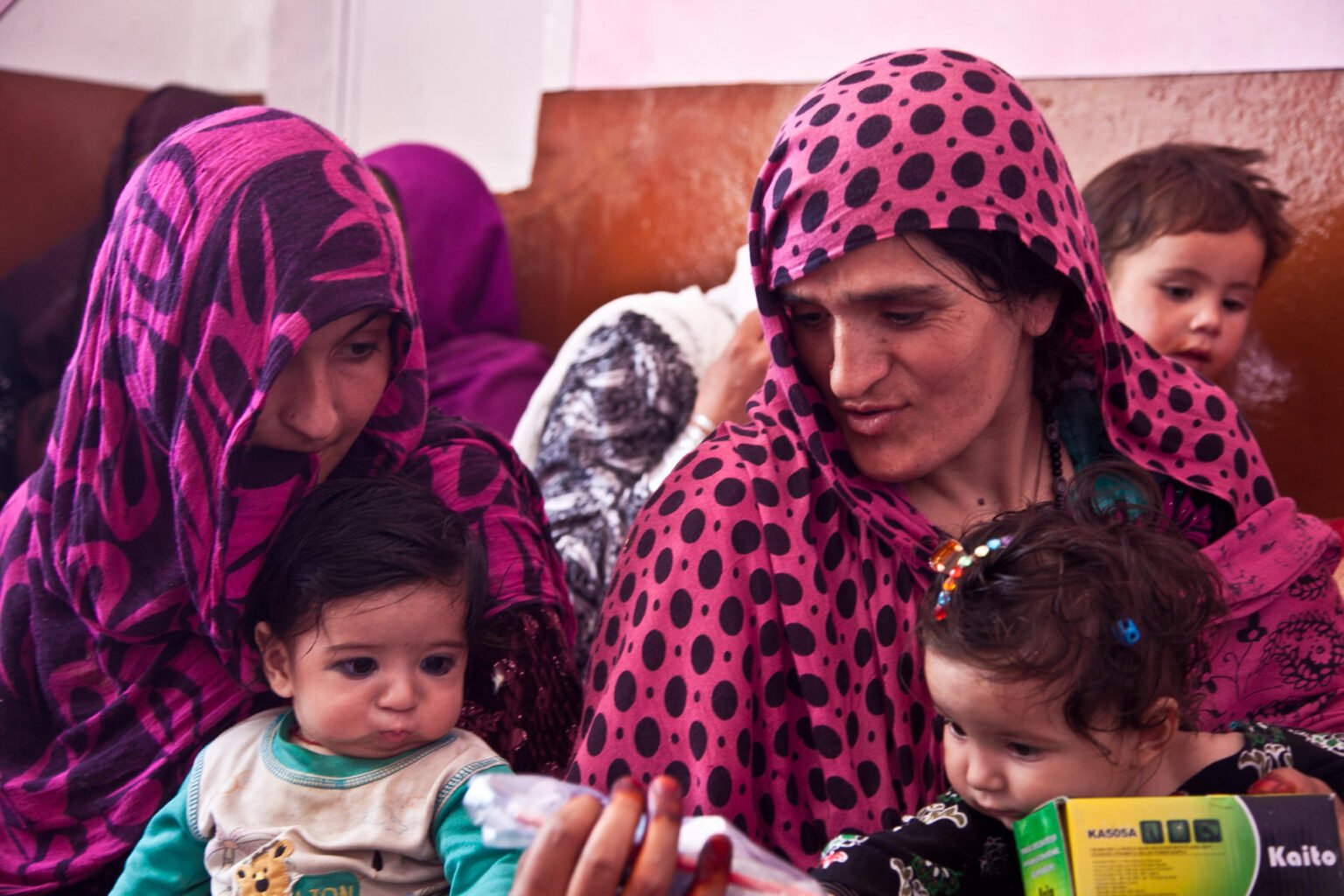 Afghan women and children at a medical seminar in Ghazni province in 2013, getting advice on hygiene products and women’s health. Such a scene would be nearly impossible under the Taliban. Photo: PJF Military Collecton/Alamy

				
				
				
				
				Farah, 25, based in Parwan province, supported her family as a civil servant and for UN agencies before the Taliban took over. Then, like so many other women, she lost her job. She did not take that sitting down and instead became involved in a centre to directly help women. But it was soon shut. Today she has no job and an increasingly unwell mother. She writes poignantly here about her life and how she continues to foster hope for herself, her family and all Afghan women despite the many challenges.
I am an Afghan woman, born in the spring of 2000 into a family where education was not merely a choice – it was the cornerstone of life itself. In our home, books were sacred, and the pen symbolised a future brighter than circumstance. My father was a doctor, a man who believed profoundly that knowledge could reshape not only an individual’s life but the destiny of an entire nation. My mother, patient, resilient, and steadfast, was a homemaker whose serene presence masked a boundless inner strength. We were eleven children, a large family with even larger dreams.
My childhood was still imbued with innocence and play when tragedy struck. I lost my father to a heart attack. The warmth and security of our home evaporated overnight. The man who had been our protector, guide, and provider was suddenly gone. From that moment, my mother assumed every role – mother, father, guardian, and pillar of strength. She began sewing clothes by hand late into the night under dim light, her hands moving tirelessly so that we could study by day. Poverty never deterred her. She would say, “Your true wealth is your knowledge. No one can ever take that from you.”
In the spring of 2019, a life-changing opportunity emerged. Dunya University, one of the most reputable institutions in central Afghanistan, announced 600 full scholarships. Its curriculum was entirely in English and aligned with international academic standards. Professors from its main branch in Switzerland taught both online and in person. For a girl from a large, resource-constrained family like mine, this was more than a chance – it was a beacon of hope.
My mother saw the announcement on television. Despite financial hardships, she borrowed money from my aunt to cover the registration fee and brought me to the entrance exam the very next day. Candidates from all 34 provinces of Afghanistan competed. When I received the call informing me that I had been accepted into the Faculty of Economics, it was as if a light had pierced through years of uncertainty. For the first time, I saw pride and relief illuminate my mother’s eyes.
University life was far from easy. In the first two years, I neither owned a smartphone nor had stable internet access. There were times when I walked long distances merely to find a spot with brief connectivity to submit my assignments. Simultaneously, I worked six hours a day at a private school as an administrative assistant. The salary was modest, yet it contributed to our household needs. Exhausted yet determined, I would return home each night to continue studying, convinced that education was the only path to secure both my future and my family’s well-being.
In late December 2020, I took the competitive examination for a governmental post at the National Statistics and Information Authority (NSIA) and was appointed to the civil service position responsible for ID distribution. My proficiency in computer skills and English enabled me to receive promotions relatively quickly. The salary I earned provided me with my first true taste of financial independence, and I remember handing the first paycheck to my mother with tears of joy in my eyes. It was a moment of triumph—proof that perseverance and education could transform one’s life.
Yet, following the political upheaval in Afghanistan, everything changed. Work conditions, regulations, and security were drastically altered. My office was relocated to the remote district of Estalf, two hours away from the city centre. New restrictions on women travelling without a male guardian rendered commuting nearly impossible. Hours were spent waiting for transportation that often refused to carry unaccompanied women. Many times, I walked long distances to reach my workplace. My feet would ache, yet the deepest pain was in my heart – knowing that I was penalised merely for being a woman.
For two months, I persisted despite immense pressure. One day, when my mother was ill, I had to traverse the two-hour journey alone on foot. Upon reaching the office, I received a message requesting that I nominate a male family member to assume my responsibilities. At that moment, my identity, competence, and hard work were dismissed. My father had passed years ago, and my brothers were still children. Reluctantly, I had to relinquish my post.
Refusing to succumb to despair, I dedicated myself to humanitarian projects. I became a community outreach officer in Parwan province, volunteering in remote villages where women had never had access to education. I encountered girls who had been forced into child marriages as early as thirteen or fourteen, and many had no basic knowledge of menstrual hygiene. I distributed sanitary pads to adolescent girls and women, often explaining proper usage, as some had never seen such resources. Witnessing their lack of awareness and vulnerability was profoundly heart-wrenching. These were lives that should have been nurtured with opportunities, not constrained by societal neglect.
During a visit to the village of Ustama, women looked at us in disbelief. They confessed that they had long been told that women should not speak, should not study, and should remain silent. Seeing us, providing education and guidance, was nearly incomprehensible for them. That moment underscored the reality that deprivation in Afghanistan is not solely economic; it is the denial of knowledge, awareness, and self-agency – a far more insidious form of oppression.
Later, I joined a project under UN Women as a Safe Space Officer. The centre became a sanctuary for women and girls. Hundreds attended daily, participating in digital literacy classes, life skills training, sewing, embroidery, painting, and small business workshops. We provided the necessary materials to enable participants to create products and link them to markets, thereby earning their own income. Witnessing the first earnings of these women – their proud smiles and newfound confidence – was profoundly inspiring. I documented their successes, recording the moments of triumph with my camera. Every snapshot was a testament to resilience and hope. The centre was not just a place of learning; it was a beacon of empowerment.
However, in late August 2024, the centre was abruptly closed by government authorities. We were expelled under accusations of teaching a “foreign language” and allegedly encouraging women to oppose the government. The office was sealed and locked. Once again, I found myself unemployed, silenced, and stripped of the opportunity to teach.
Days later, a young participant called me, eager to know when classes would resume. I had to convey the bitter truth: the programme had been terminated. I could hear her sobs through the phone. A few days later, her mother informed me that the girl had taken her own life. The news shattered me. I wrestled with guilt and depression for months, haunted by nightmares of those I could not protect.
Although I understood that systemic oppression, not personal failure, was the cause, the grief was almost unbearable.
Today, my mother lives with chronic heart disease and diabetes, with three stents in her heart. At times, being unable to procure her essential medication brings me to the brink of despair. Yet, despite all hardships, my hope persists.
I share this story not to elicit pity, but because the voices of Afghan women deserve to be heard. My goal is to reclaim the right to education, to work with dignity, and to empower other women to realize their potential. Wherever I am, I strive to contribute to a future in which no girl must bury her dreams because opportunities were denied to her.
Though doors may be closed today, hope remains alive. As long as hope endures, the struggle for dignity, justice, and equality will persist.
Farah         

			
			
					
				
				
				
				READ MORE