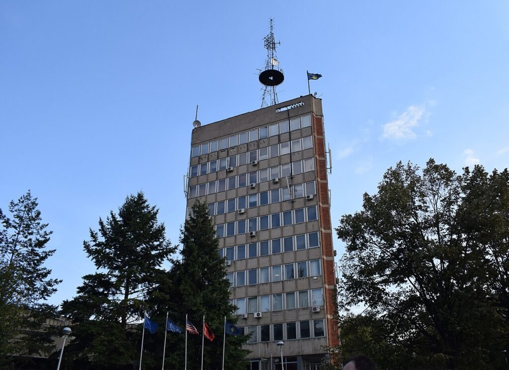 Funding of just 8.9
million euro would  only be sufficient to cover RTK’s basic operational needs. Photo: Arianit/CC BY-SA 4.0

				
				
				
				
				The undersigned international media freedom and journalist organisations today express our serious concerns about the underfunding of Kosovo’s public broadcaster, Radio Television of Kosovo (RTK), and urgently call for legal budget requirements to be met.
The Assembly of Kosovo is currently discussing the RTK budget, which is anticipated to be passed in two readings on 19 and 20 February 2026. According to the draft Law on the Budget for 2026, the parliament, based on the government’s proposal, will allocate only 8.9 million euros, which is sufficient only to cover basic operational needs such as staff salaries.
The Law on RTK foresees that the public broadcaster should receive 0.7 percent of the total state budget of around three billion euros. This would mean that RTK should be allocated approximately 22 million euros. If passed, the current budget would be only 40% of this legally mandated total.
A budget shortfall of this scale would seriously undermine the ability of the public broadcaster to operate independently and to fulfil its mission to inform citizens on matters of public interest. If RTK were to receive the budget it is legally entitled to, it would allow it to operate independently from any interference from the government and Parliament, while also enabling investment and development of the public broadcaster.
We note that Article 5 of the European Union’s European Media Freedom Act (EMFA) requires Member States – which Kosovo aspires to become – to provide sustainable and adequate funding to public service media to allow for their stable and independent operations.
The proposed budgetary system, which conflicts with the existing legal framework, would, if applicable, clearly violate this EMFA provision. We take this opportunity to invite the Government and the Parliament to initiate work on the implementation of the EMFA, as well as to begin discussions on reforming the funding and governance of RTK to ensure that its editorial and functional independence is guaranteed.
Ahead of the pending budgetary decision, our organisations therefore jointly ask the Prime Minister and President of Lëvizja Vetëvendosje, Albin Kurti, and the Speaker of the Kosovo assembly, Albulena Haxhiu, to ensure that the public broadcaster receives the adequate and equitable budget in accordance with the law and that it is not subjected to political pressure through budget limitations.
Signed:
European Centre for Press and Media Freedom (ECPMF)
International Press Institute (IPI)
European Federation of Journalists (EFJ)
Index on Censorship
Osservatorio Balcani Caucaso Transeuropa (OBCT)

			
			
					
				
				
				
				READ MORE