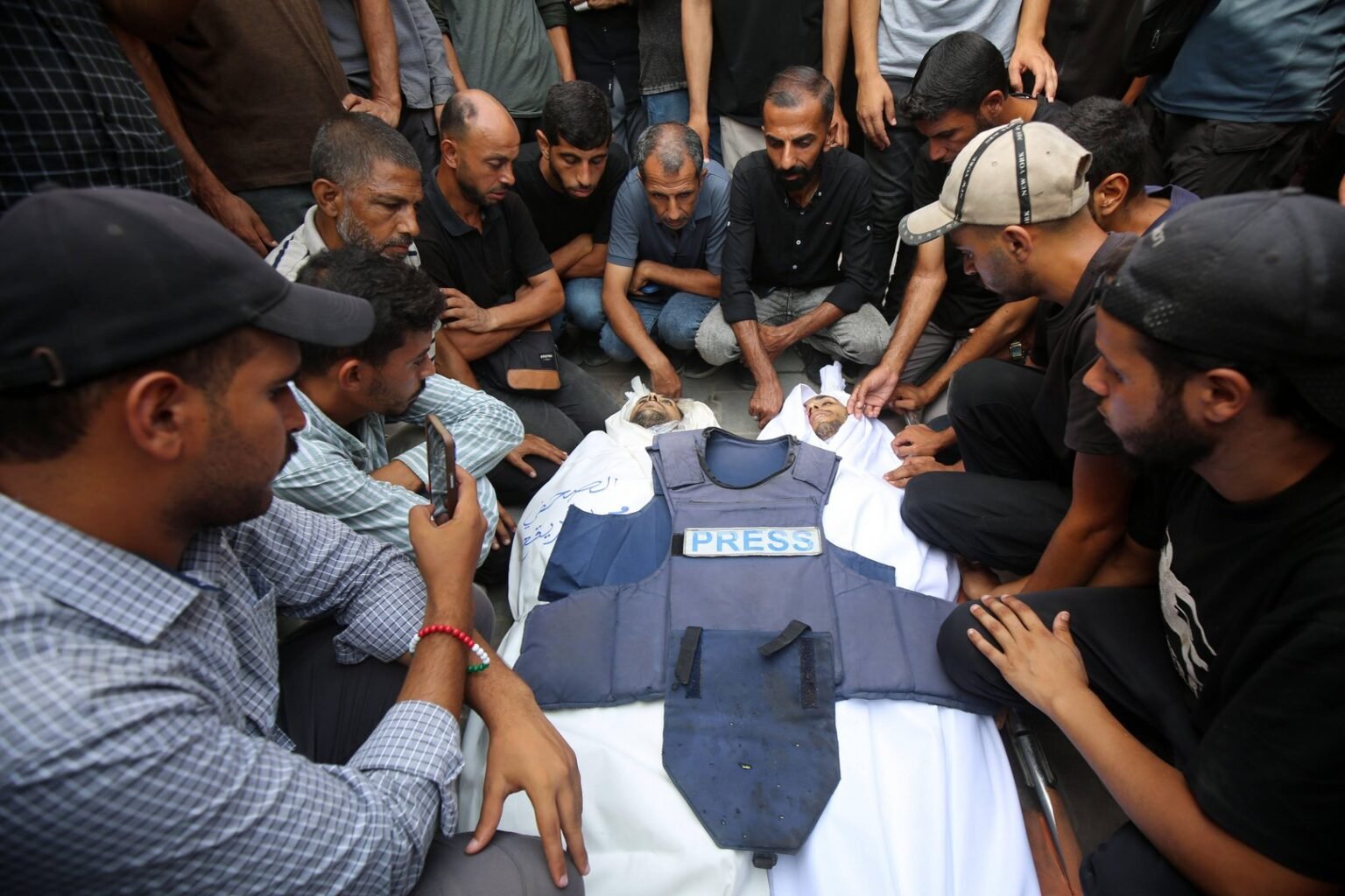 Mourners carry the body of Al Jazeera correspondent Anas al-Sharif, who was killed alongside other journalists in an overnight Israeli strike on their tent in Gaza City, during his funeral in Gaza City on August 11, 2025. Photo: IMAGO/Omar Ashtawy apaimages/Alamy

				
				
				
				
				JAMES CAMERON MEMORIAL LECTURE 2026 – MARCH 4, 2026 – LONDON
It is January 2000; an aspiring student journalist is on a two-week work placement in Plymouth.
She writes stories on local music concerts, mix-ups over the introduction of the metric system for selling fruit and vegetables, clashes between local school sports teams, the building of a new community centre. She interviews strangers in the street about their favourite books as part of a nationwide survey and for their views on dentists. She covers sports, politics, arts, charity, business. And she knows, as she has known since she was six years old, that all she wants to be is a journalist.
It is January 2026. A photographer heads to cover protests in Minneapolis in the United States. As he tries to live stream and take photos of the crowd that has gathered to protest immigration enforcement in which a protestor was shot dead, he is tackled to the ground by immigration officers and pepper sprayed. He is handcuffed and arrested. And in that moment, the moment when he is hurled to the ground by officials in combat gear, clutching a face mask he’d bought in a local hardware store to protect himself from tear gas, the photographer thinks only of one thing. He must protect the images he has captured of these events – and he throws his camera out from under him in the hope someone will save it.
The journalist in Plymouth, on a two-week placement with the Evening Herald, was me. Then a postgraduate diploma student here at this very university. The photographer is John Abernathy, one of hundreds of journalists in the United States now grappling with a surge in violence against the profession.
We dreamed a lot of dreams when we were at City. I dreamed of being the Director General of the BBC. A friend of being the Editor of The Sun. Some wanted to be political reporters, others sports, some wanted to write about arts and culture, others economics and finance. We knew that over the years many would leave the profession. Some went on to great success in the very careers they envisaged, others took unexpected turns into academia, the civil service, and entertainment.
But what none of us could have predicted was how radically the environment would change for the profession itself. That the kinds of preparations journalists used to undertake to cover war zones would be needed to cover protests in North America. That journalists covering Westminster or the White House would regularly receive death threats. That a journalist in a European Union country might be killed for their investigative reporting.
But that is what has happened. Now, this moment, is the most dangerous time in recent history to be a journalist. Last year, a record 129 journalists and media workers were killed worldwide, the highest number ever in the more than 30 years that the Committee to Protect Journalists has been documenting such data. For the past three years, more than 300 journalists were in jail at the end of the year – including in countries that are supposed democracies. Journalists are subjected to daily online harassment, including threats of death and rape. They are smeared by those in power and mistrusted by those without it.
And yet – although this is the worst time in the world to be a journalist – it is also the most important time.
Today, I want to examine why journalism has become so devalued, why journalists have become so demeaned, and why those whose job it is to deliver facts, to speak truth to power, to expose corruption and injustice, are now in greater peril than at any time in recent history. I also want to share what we can do about it.
And why – if we want to live in anything approaching fair and just societies, ones that uphold rights and freedoms for all – it is essential that we step up to defend a free press — in deeds not just in words.
First, let me tell you a little bit about the Committee to Protect Journalists, the organisation I now lead. Based in New York, the Committee to Protect Journalists was founded in 1981 to defend press freedom and journalist safety worldwide. One of our first advocacy campaigns was in support of three British journalists arrested in Argentina while covering the Falklands War. A letter from then CPJ Honorary Chairman Walter Cronkite helped spring them from prison.
Sadly, the days when a letter and a stern word could provoke such a result are long gone, so CPJ now works in three ways:
• We research and document threats to press freedom globally,
• We provide direct assistance to journalists at risk,
• And we advocate on behalf of those targeted for their work.
Last year, we provided more than .3 million in direct financial assistance to journalists needing emergency support, covering everything from the cost of legal fees for reporters wrongfully imprisoned for their work, to medical bills and trauma support for journalists attacked and harassed in retaliation for their reporting, to exile assistance. We reached an unprecedented total of 3,877 journalists last year – more than 5 times the number of the previous year.
It’s no surprise those numbers have grown – because attacks on the press have grown exponentially in the past decade. In 1992, when CPJ first started systematically documenting attacks on the press, 56 journalists and media workers were killed. Last year’s number is more than double that. In 1992, there were 113 journalists in jail. Last year’s number is more than triple that.
In 1992, Mark Zuckerberg was 8 years old, the launch of Google was still six years away, and Facebook and Twitter would not emerge for more than another decade.
Now, the internet and social media dominate communications, and online harassment – especially of women and those from marginalised communities – is rife. Let me give you one recent example. In 2023, Sabrina Schnur, a young female reporter at the Las Vegas-Review Journal in the United States wrote about the hit-and-run killing of a retired police chief. Schnur was the first journalist at the scene after the killing and also the first local reporter to talk to the police chief’s family. But after screenshots of a month-old obituary sparked accusations the Review-Journal was downplaying the death, Schnur was subjected to a slew of hate-filled abuse. Her email inbox and social media mentions were flooded with personal attacks. She was accused of being anti-white. Her photo was shared, and her office phone number circulated. The attackers hurled antisemitic abuse at Schnur, told her they hoped she would get cancer, that she would die. They found her private social media accounts and unearthed posts she’d made as a teenager, going as far back as 2015.
Schnur and her colleagues had more reasons than most to be concerned about online threats. A year earlier one of the Review-Journal’s leading reporters – Jeff German – was stabbed to death by a local official who was the subject of German’s reporting. The suspect first targeted German with attacks on social media.
How did we get here? Not by accident.
The decline in press freedom and journalism safety is directly tied to a decline in democratic norms and a rise in authoritarianism that we are experiencing worldwide. And no wonder. Autocrats and demagogues have long known that to control a population, you need to control the flow of information to that population. Targeting the press is the first step to stifling dissent.
If we want to tackle this, we need to understand the playbook for attacking the media, which in essence goes something like this: Smear, Harass, Criminalise, Kill.
Let’s start with smearing. This is one you may be familiar with. Name calling may feel like the petulant act of the playground bully but it’s remarkably effective. Hungary’s leader Viktor Orbán does it, smearing the press as “fake news,” former Filipino President Rodrigo Duterte did it, calling them “presstitutes”, US President Donald Trump does it, calling journalists “enemies of the people” and most recently calling one journalist “piggy” and telling another who asked him about his ties to Epstein to “smile”.
More insidiously, we are increasingly seeing a tendency to smear journalism itself as a nefarious act – think of the way in which the US Secretary of Defence conjured images of journalists roaming the Pentagon as a security risk. What Pete Hegseth of course conveniently forgot was that journalists have operated successfully from the Pentagon for decades, while it was Hegseth himself who shared secure information about military plans on a Signal chat group in which a journalist had been mistakenly added. Rather than be seen as critical work in the public interest to expose abuses of power, journalism itself is being rebranded as a subversive act.
Smears escalate. By setting the tone at the top, those in power create a permission structure for harassment. Sometimes that might be formally orchestrated by those in power, more often it develops organically, among their supporters and sympathisers. Diaspora news outlet, The Haitian Times, for example, received a slew of racist abuse after it reported on the false claims made during the US presidential campaign about Haitians eating pets. In a demonstration of the online to offline risks, one reporter even had police show up at her house after a false report was made about a crime being committed there – a practice known as swatting.
Harassment does not just take the form of online or even physical abuse. It can be legal and regulatory as well. This includes the use of so-called SLAPPs – vexatious lawsuits that are designed to drain journalists and media organisations of money and morale. At the time of her murder in 2017, investigative Maltese journalist Daphne Caruana Galizia was facing 47 such suits. In July last year, CBS owner Paramount settled a case that legal experts widely agreed was spurious for  million – a case brought by none other than the US President himself. Weeks later the US broadcast regulator, the Federal Communications Commission, approved a multi billion dollar merger involving Paramount.
Harassment can also take financial form. Cutting funding or using public money to favour political friends and punish political enemies has long been a tactic of autocrats but we increasingly see this in democracies. Since Trump took office, his administration has all but eliminated funding for publicly funded media, mostly impacting local, regional broadcasters serving rural communities, as well as effectively shuttering Voice of America, Radio Free Europe and Radio Free Asia – all services that provided information to and about countries where media freedom is severely curtailed.
So, smearing, then harassment. These are steps one and two.
But it does not stop there. Because mud sticks. Demeaning journalists, branding them as cheats and liars paves the way for the third factor that is common to this playbook: actually criminalising journalism and journalists. Nobel laureate Maria Ressa has spoken extensively about the way branding of journalists as criminals by those in power helps soften the public up for subsequent actual criminalisation and arrest – and of course even killing. Years before the state launched lawsuits against her, the Philippines was readying the public to believe she was an actual criminal by painting her as one.
Dubbing journalists as criminals is a deliberate strategy intended to sow doubt in the mind of the public about their trustworthiness – and therefore about the trustworthiness of their information. It’s a means to control the narrative.
But criminalising journalists is not just about controlling public perception. It’s also used as a means to silence individual journalists – and to send a warning to other reporters and news outlets.
It is a tactic used increasingly, even in supposed democratic regimes. Take the example of Hong Kong where 78-year-old British citizen Jimmy Lai, founder of the independent Apple Daily newspaper, was given a 20 year jail sentence. Lai has been in jail in Hong Kong. Largely in solitary confinement, since 2020 on numerous charges, including sedition and collusion with foreign forces for having the temerity to publish a newspaper that covered pro-democracy protests. In Guatemala, José Rubén Zamora, who for decades has exposed government corruption in his country, was recently released from jail in Guatemala where he faced trumped up charges of money laundering. In both cases, the legal teams for these journalists have themselves faced targeted harassment and threats – and in both cases the newspapers they founded have been forced to shutter as a result of legal action.
And, of course, we have seen this over and over again in Gaza, where Israel repeatedly smears journalists as terrorists and militants, without providing evidence – as a way to justify subsequently killing them.
Killing journalists is the ultimate form of censorship. And no discussion of journalist safety in the current moment can avoid what has been the deadliest assault on journalists since CPJ began. Of the 129 journalists and media workers killed last year, 86 were killed by Israel. The majority of them were Palestinians. Israel has now killed more journalists than any other government since CPJ began collecting records in 1992, making the Israel-Gaza war the deadliest on record for journalists. And let’s be clear. These are not the ordinary casualties of war. In at least 38 cases documented by CPJ last year alone, we believe journalists were deliberately targeted. This includes Al Jazeera reporter Anas al-Sharif, whose life CPJ publicly warned was in danger after repeated, unsubstantiated smears by Israel against him. Following years of such threats, Al-Sharif was murdered on August 10, alongside three other Al Jazeera staff journalists and two freelancers in a strike on a tent housing reporters. Journalists are civilians. Deliberately targeting them constitutes a war crime.
The magnitude of Israel’s killings is exceptional, but – worldwide – the killing of journalists, the smearing of journalists, the harassment, the legal threats, the financial punishments – these are no longer an exception.
Ok. So at this point, you may be shrugging your shoulders and saying, “Who cares?” Maybe you think the media brought it on themselves. Maybe you hate the “lamestream” media and think we all deserve to be smeared, harassed and attacked.
I want to tell you why it matters.
It matters because information is a prerequisite for free and open societies. Attacks on journalists are the first sign of democratic decline. Study after study shows that attacks on journalists matter because they are a clear indicator that attacks on other rights, our rights, will follow.
It matters because journalism is essential for our everyday lives. Without it, we don’t have the information about the decisions being made by governments in our name or how our taxes are being spent. We don’t have information that might help keep us safer or healthier or might help stop abusive practices.
It matters because journalism is essential if we want to understand the world. In Gaza, it is Palestinian journalists who have been our eyes and ears for two and a half years so that we can understand what is happening there. With no independent international access allowed since October 7, it is local journalists who are bearing witness to the genocide that they are also living through.
Journalism is essential if we want to understand our own country. In the UK, it is journalists who have repeatedly uncovered government scandals. Journalists like my friend, former City alum, and multi award winning journalist Pippa Crerar, who – among other things – exposed the Partygate scandal. Harriet Harman, who chaired the parliamentary investigation into Partygate praised Pippa’s journalism in the Commons, saying: “This episode has shown that wrongdoing has not gone undiscovered and attempts to cover it up have failed, but it would have been undiscovered had not the press doggedly investigated.”
Journalism is essential because reliable, fact-based information can save lives. When wildfires broke out in California at the start of the year, local residents turned to local media for information about the outbreaks: about where was safe, how the fires were moving, what precautions to take. In many rural parts of the United States, there is no reliable internet. Local radio is the most important source of information, especially in an emergency. In rural Alaska, it is the local independent radio stations who are tasked with providing early warnings of tsunamis and extreme weather – stations whose funding has been gutted by federal cuts.
In the absence of independent, reliable fact-based media, a vacuum is created. One that is easily filled with lies, half-truths and propaganda.
We cannot afford to be complacent. Journalism has value, it has impact – and yet journalists are being killed at a faster rate than in any other time in recent history, journalists are being jailed in higher numbers than at any other moment in recent history. News deserts – places with no access to credible news and information about their local community – are spreading. Funding for independent journalism in and about countries with little or no media freedom has been slashed.
So, if we know journalism has value and if we know that it is under attack like never before, what are we going to do about it?
Well, firstly, we need to accept that current ways of operating are failing and we need to look for new ones.
One example of this is impunity. It is widely recognised that impunity – a failure to punish those responsible for attacks on journalists – creates environments that allows further attacks – more egregious, more violent attacks – to persist and flourish.
More than a decade ago, the United Nations established the International Day to End Impunity for Crimes Against Journalists as an effort to draw attention to this fact. Each year for more than a decade we at the Committee to Protect Journalists would publish a report on the worst offenders – the countries where most journalist murders had gone unpunished. And yet the numbers remained stubbornly and persistently high.
So, instead of thinking about what everyone else needed to do to address this, this year we took a look at ourselves.
And that’s why on International Day to End Impunity this year, CPJ decided to drop our annual Impunity Index. Measuring which governments were – literally – getting away with murder was a useful way to shed light on the issue a decade ago, but it’s no longer enough.
We are overhauling our approach to focus where we know we can have impact and on new initiatives that hold promise.
These initiatives include:
Firstly, pursuit of justice in key cases. Our experience in the past decade has shown that one of the most effective mechanisms for tackling impunity is a relentless pursuit of justice in individual cases. Going forward, CPJ is dedicating increased resources to a select number of such emblematic cases, supporting families and local communities in their often-lengthy fights to continue investigations and prosecutions.
Secondly, we are pushing for the establishment of a standing independent international investigative task force focused on violent crimes against journalists. Relying on perpetrators of crimes against journalists to lead investigations into those crimes and hold those responsible accountable will always make ending impunity an uphill if not impossible battle. We need an independent global body readily available to support investigations – local, regional or international – into attacks.
Thirdly, we need to see increased accountability from companies. Businesses play a key role in enabling attacks on journalists. CPJ is stepping up its focus on investigating and seeking accountability over the use of companies’ technology in cases where journalists are targeted or harmed. The increased use of drones is likely to be a particular focus in 2026.
We asked ourselves, “What can and should we be doing in this moment?” and it is a question we must all ask ourselves.
So here are some things you can do as an individual:
1. Spend money! Invest in local media
The evisceration of local media has been credibly linked to worsening outcomes for communities, including loss of community cohesion, lack of oversight and accountability leading to poor spending decisions, increased corruption, and even rising local taxes.
If you don’t already, do it, go out today and subscribe to your local news outlet. Or someone else’s. When the Kansan local newspaper the Marion Country Record in the US was wrongfully raided by police a few years ago, subscribers flooded to support the outlet – including many who lived hundreds of miles away. One Florida man told the Record’s editor he subscribed because he’d read local newspapers as a boy and missed the sense of community (2,500 kms away).
2. Lobby your local authorities and governments, and your employers!
It is not enough for governments to say they support a free press. They need to demonstrate this in practice, both at home, and in their dealings with governments abroad – and they need to know their constituent’s care.
As voters, we can ask our elected representatives to make these issues a priority.
As employees, we can ask our employers to make this a priority. If you are an academic, does your university have programs for exiled journalists/ journalists at risk? Do your professional journalism courses include safety modules as standard? If you are a journalist, does your employer provide digital health checks or privacy tools? If the answer to these questions is no, ask for them. I can help you…
3. Let’s do our jobs as journalists.
When I started at CPJ three and a half years ago, the motto of the organisation was “using the tools of journalism to protect journalists.” To be honest, as a former reporter, I somewhat scoffed at this description. After all, we are not a news agency. We are not a newspaper of record. We are an advocacy organisation. But over the past three years, as I have watched our profession fail over and over again in its coverage of Gaza, I have come to realise how important it is for all of us to recommit to, and publicly champion, the core principles of good journalism. It is the very essence of good journalism – the ruthless pursuit and public dissemination of facts – that will be our strongest defence.
Recentring facts means explaining how we got them and why they matter. One of the reasons I would argue that journalists have suffered such a loss of trust in recent years – quite apart from some clear and obvious failures, including illegal phone hacking here in the UK – is that we assumed people understood what we did and what value we had. But as more and more individuals claim to be journalists or news outlets claim to be conducting journalism, those who are engaged in actual journalism – reporting to establish facts – need to do more to show how they arrived at the information and why they should be trusted.
Recentring facts also means celebrating your impact. When I became a reporter, I was told time and again that journalists didn’t like to report on ourselves. That reporting on issues facing the industry could be considered self-indulgent. But if we want people to understand the worth of journalism, we must report not just the news, but how and when our reporting has effected change.
Let’s be half as brave as our colleagues who risk everything to report the truth. I was asked in a recent interview what message I had for Western journalists covering Gaza. My response – although in slightly more colourful language – was “Do your job.” The job of a journalist is not that of a parrot – it is not simply to ask questions and rehearse what we are told. That’s not fact finding. That’s stenography. Our job is to dig deeper, to see with our own eyes and hear with our own ears where possible, and – if not possible – to gather as much information from as many sources as possible to establish the truth.
Instead of worrying about being perceived to take sides, our responsibility is to report the facts. It requires courage. Cowardice is the enemy of good journalism. George Orwell had this right back in his original proposed preface to Animal Farm. “Obviously,” Orwell wrote, “it is not desirable that a government department should have any power of censorship… But the chief danger to freedom of thought and speech at this moment is not the direct interference of the MOI or any official body. If publishers and editors exert themselves to keep certain topics out of print, it is not because they are frightened of prosecution but because they are frightened of public opinion. In this country intellectual cowardice is the worst enemy a writer or journalist has to face, and that fact does not seem to me to have had the discussion it deserves.” Animal Farm was published in 1945. What Orwell wrote then is as true today: our job as journalists is to stand up to the bullies – not to bow to them. That’s what CPJ wrote to Shari Redstone, former chair of Paramount, when we urged her not to settle with Trump over his lawsuit against CBS. Capitulation creates a precedent – and each individual capitulation weakens the entire ecosystem.
I am by no means saying this is easy. Journalism will always be risky as will defending it. It takes a certain level of defiance – a willingness to speak truth to power, to report things as they are, as we see them, and to place them in context – even, and perhaps especially, when it’s not what people want to hear. Doing it well takes courage and conviction. In 2009, prominent Sri Lankan journalist Lasantha Wickrematunge was murdered by a group of men on motorcycles. He had been receiving threats for months but refused to stay silent about the injustices in his country. For the last decade, Filipino journalist – now Nobel Laureate, Maria Ressa has been subject to a relentless legal campaign intended to discredit, bankrupt, and ultimately silence the critical reporting coming from both her and her newsroom, Rappler. At one point, she faced a possible sentence of more than a hundred years behind bars. But Maria knows that the job of a journalist is to report the facts, not to bend to those who benefit from their burial. She refuses to stay silent.
More than 200 Palestinian journalists have been killed by Israel since the start of the Israel-Gaza war. Many have been deliberately threatened and warned explicitly by Israel to stop their reporting. All know the risks they take in wielding cameras when Israel has repeatedly targeted journalists even when wearing press vests and working from known press zones. They know that in the end facts are our superpower. They know that killing the messenger does not kill the message. So, they refused to stop. They refused to be silent. If we want to save journalists, if we want to save journalism, we all must do the same.
BY JODIE GINSBERG
CEO, COMMITTEE TO PROTECT JOURNALISTS
Editors note:
This is the alert that the CPJ put out over the weekend in response to an Israeli strike on a media car which killed three journalists in Southern Lebanon.

			
			
					
				
				
				
				READ MORE