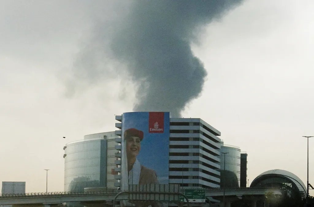 Smoke rising from an area near the Dubai International Airport is seen through the windshield of a vehicle, after a drone attack hit a fuel tank, according to Dubai authorities, on March 16, 2026.