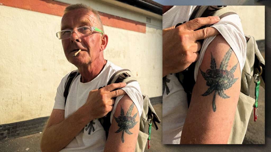 A man in a white t-shirt pulls up his sleeve to show a tattoo of a marijuana leaf on his arm.