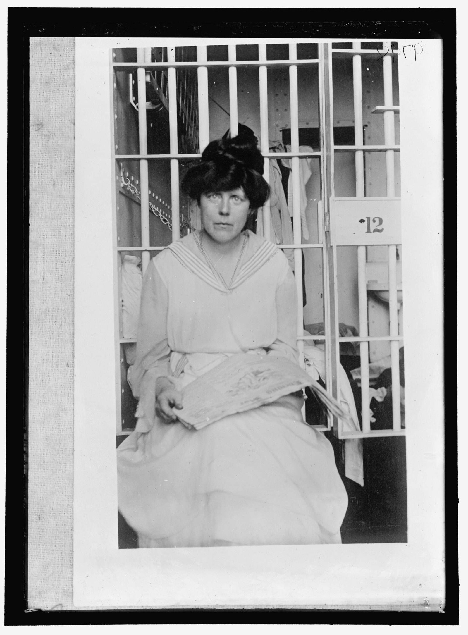 Black and white photo of a woman sitting in front of a prison cell